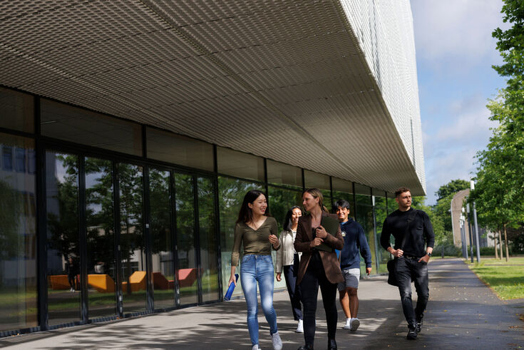 Eine Gruppe internationaler Studierender läuft entlang der Glasfassade des J-Gebäude auf dem Krefelder Campus entlang.