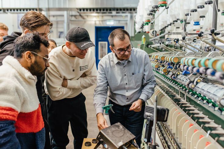 Professor erklärt Studierenden eine Spinnmaschine